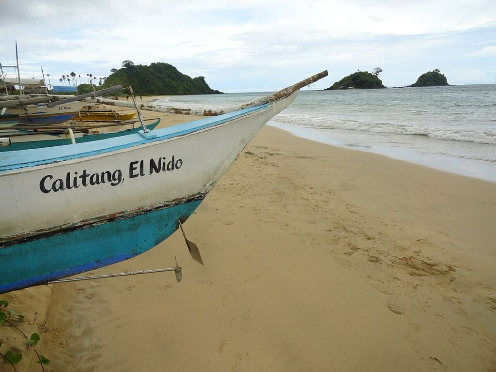 Proue d'une bangka de pêcheur sur le sable de Nacpan Beach, îlots jumeaux en arrière-plan