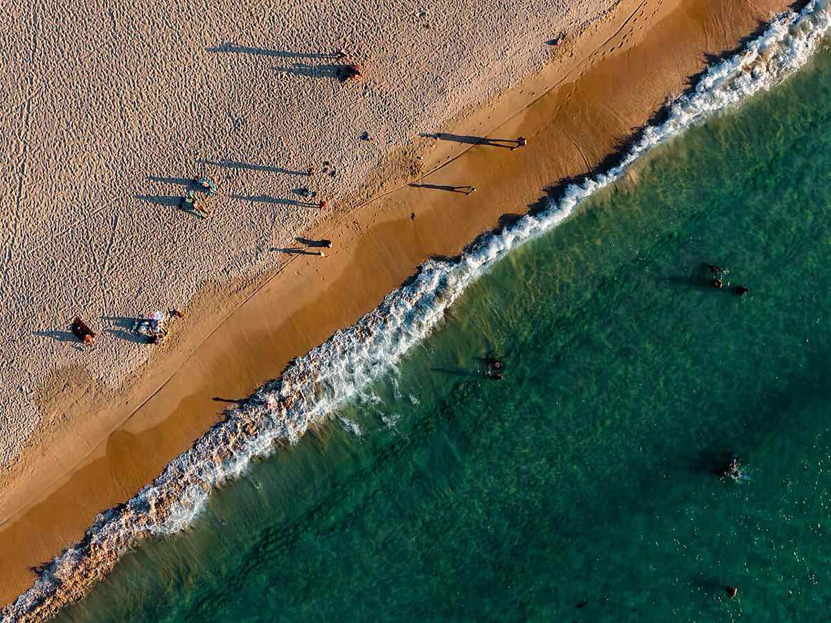Vue aérienne de Nacpan Beach au petit matin, baigneurs et ombres longues sur le sable doré